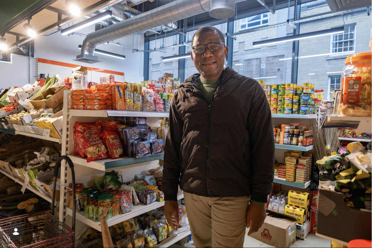 The owner of Tropikal Foods Super Store standing among well-stocked shelves of Afro-Caribbean groceries
